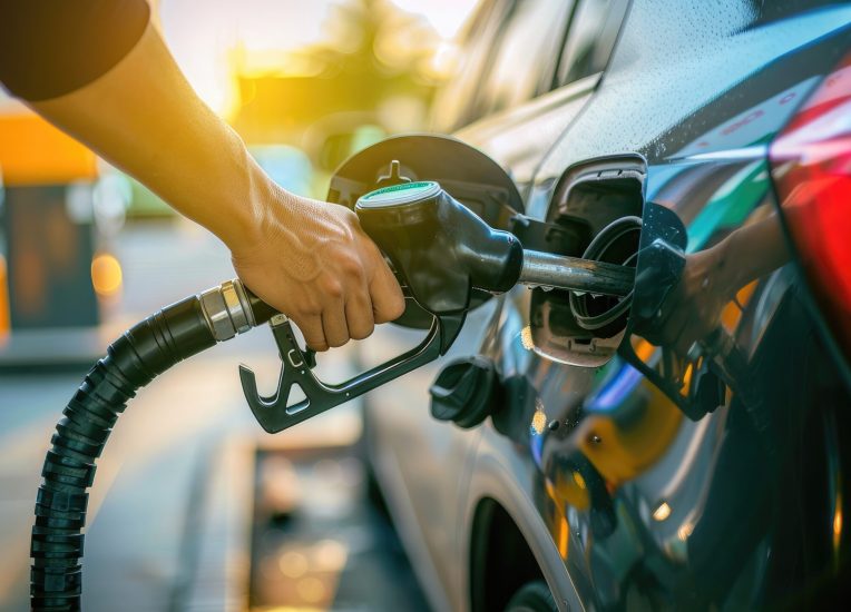 Close-up of a man's hand holding a gas nozzle and filling a car with gasoline at a gas station
